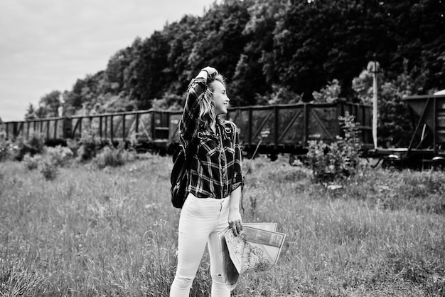 Portrait of a young blonde in tartan shirt next to the train with a map