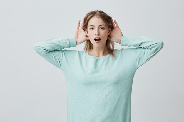 Portrait of young blonde woman holding hands behind her ears while listening to some incredible story