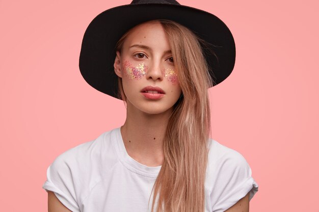 Portrait of young blonde woman with glitter on face and stylish hat