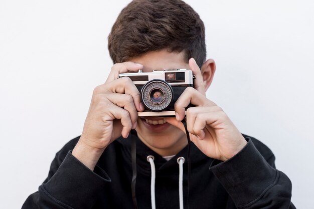 Портрет молодого мальчика фотографируя через ретро камеру на белом фоне