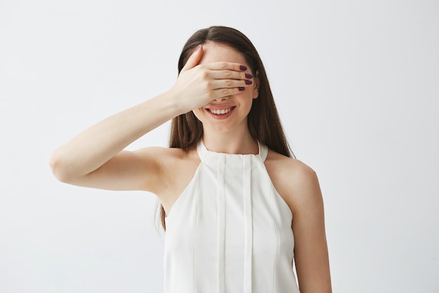 Portrait of young brunette girl covering eyes with hand smiling .