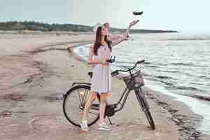 Free photo portrait of a young brunette girl in sunglasses and hat wearing dress enjoy the vacation on the beach, playing with the quadcopter.