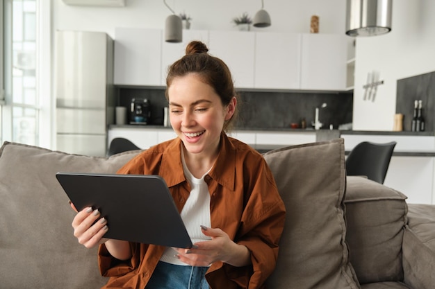 Free photo portrait of young brunette woman reading on digital tablet watching tv series on her application