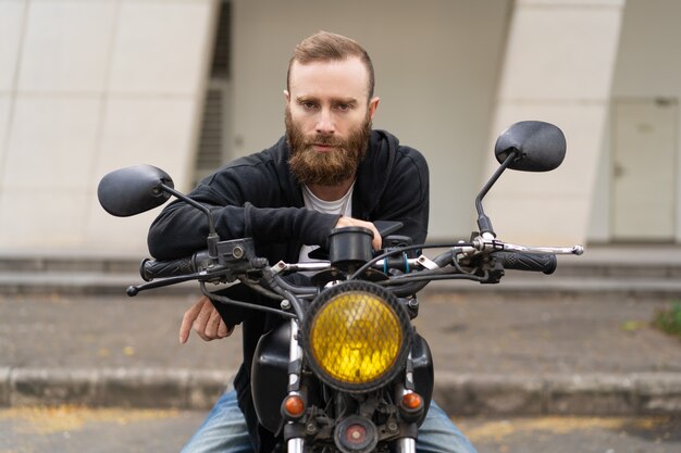 Portrait of young brutal man sitting on motorcycle outdoors