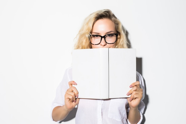 Ritratto di una giovane donna di affari che si nasconde dietro un libro con gli occhiali, isolato su un muro grigio