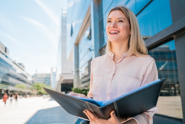 Portrait of young business woman holding clipboard while standing outdoors at the street. Business concept.