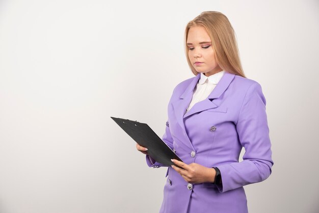 Portrait of young business woman standing and looking on clipboard.
