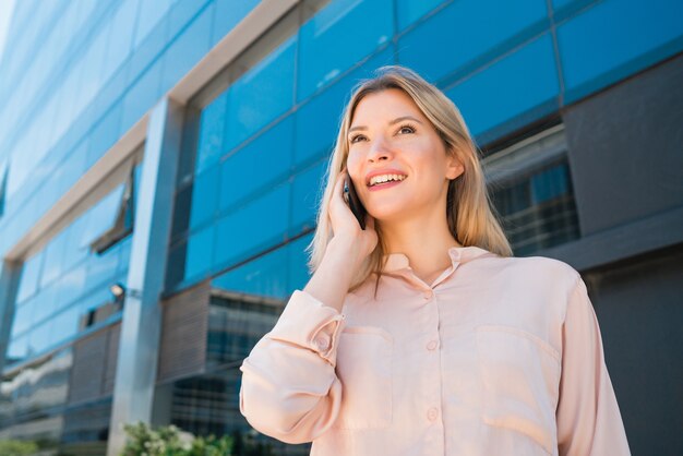 Portrait of young business woman talking on the phone while standing outside office buildings. Business and success concept.