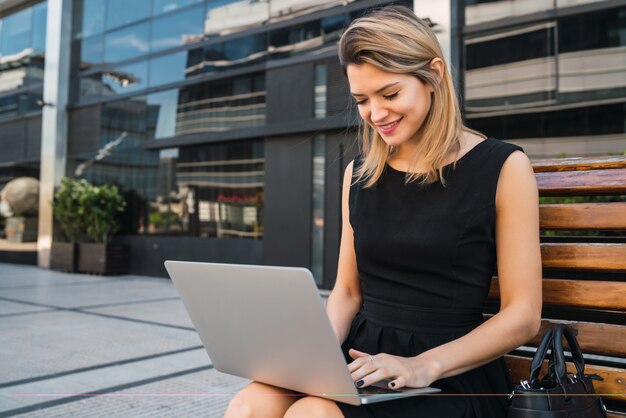 야외에서 거리에 앉아있는 동안 그녀의 노트북을 사용하는 젊은 비즈니스 여자의 초상화. 비즈니스 개념.
