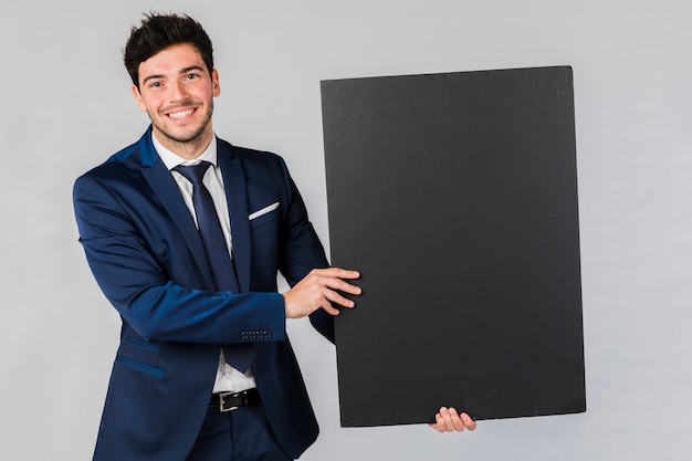 Portrait of a young businessman holding blank black placard against grey backdrop