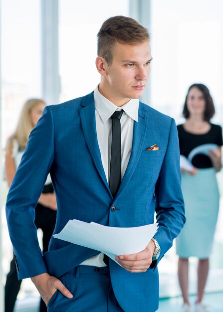 Portrait of a young businessman holding documents in office