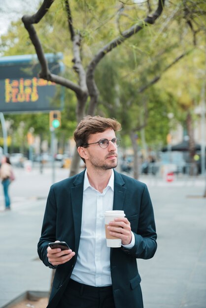 携帯電話とテイクアウトのコーヒーカップを保持している青年実業家の肖像画