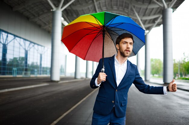 Портрет молодой бизнесмен, холдинг пестрый зонтик, ловить машину в аэропорту