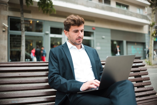 Портрет молодого бизнесмена, сидя на скамейке с помощью ноутбука