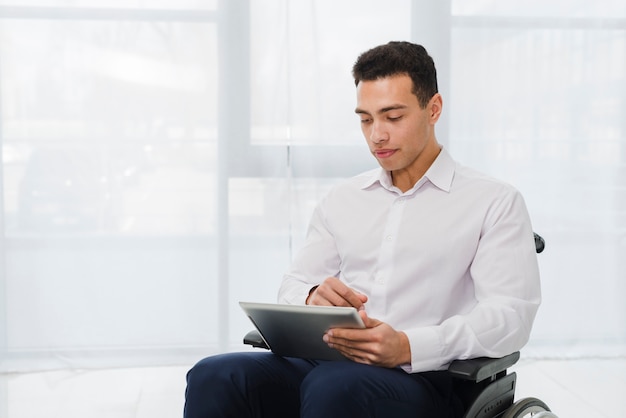 Portrait of a young businessman sitting on wheelchair looking at digital tablet