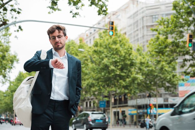 Portrait of a young businessman standing on city street checking the time