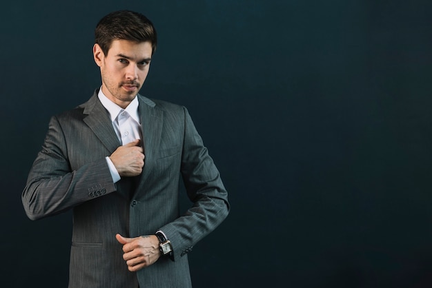 Portrait of young businessman in suit standing against black background