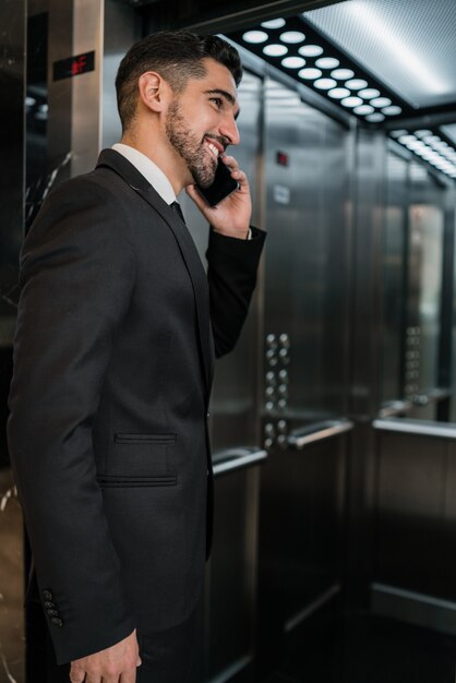 호텔 엘리베이터에서 전화 통화하는 젊은 사업가의 초상화. 비즈니스 여행 개념.
