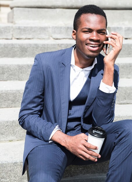 Portrait of a young businessman talking on steps holding disposable coffee cup