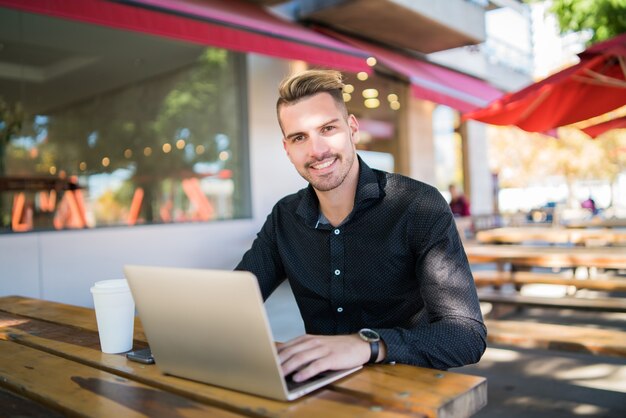 Portrait of young businessman working on his laptop while sitting in a coffee shop. Technology and business concept.