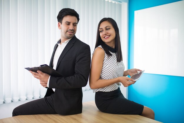 Portrait of young businesspeople sitting on table and flirting