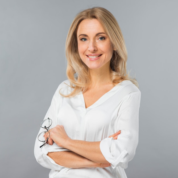 Portrait of a young businesswoman holding eyeglasses in hand against gray backdrop