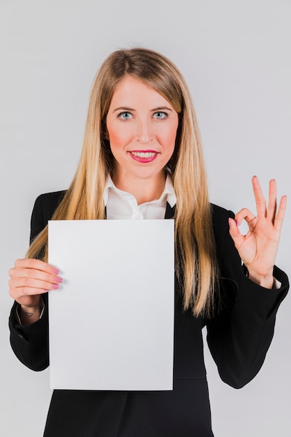 Портрет молодой коммерсантки держа белую бумагу в руке показывая одобренный знак