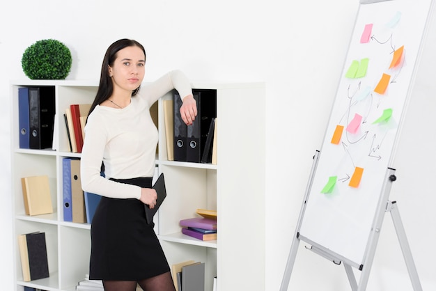 Portrait of a young businesswoman leaning on shelf at workplace