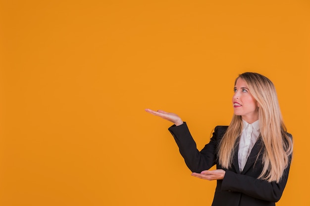 Free photo portrait of a young businesswoman presenting something against an orange backdrop