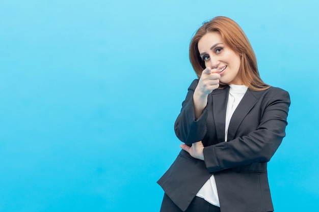 Portrait of young businesswoman standing on blue background and point her finger to the camera