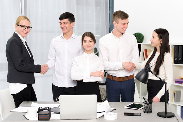 Portrait of a young businesswoman standing with business people shaking each other's hands at workplace