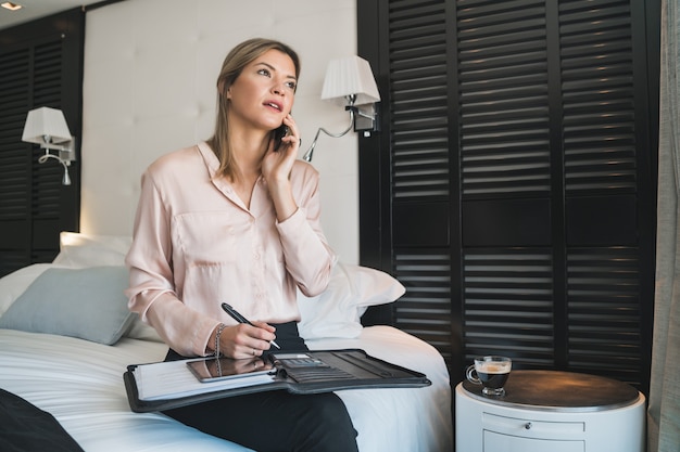 Portrait of young businesswoman talking on the phone at the hotel room. Business travel concept.