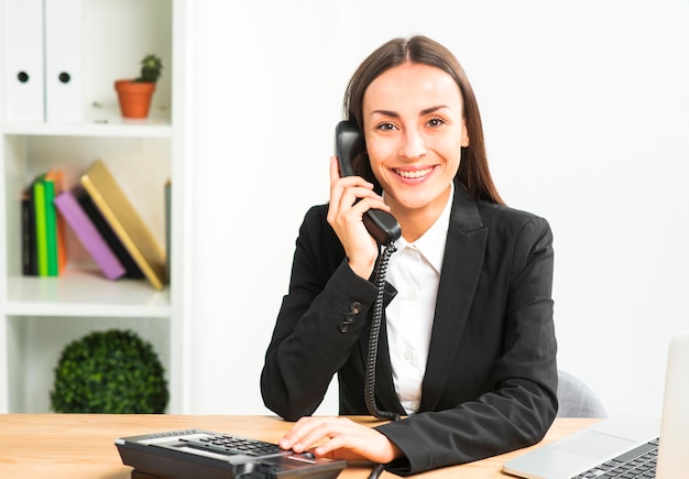 Portrait of a young businesswoman talking on telephone looking at camera