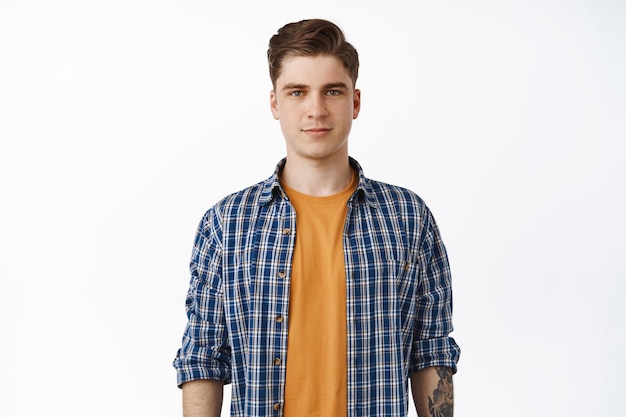 Portrait of young candid man, student boy with clean face, relaxed facial expression and casual smile, checked shirt over t-shirt, summer outfit look, white background.