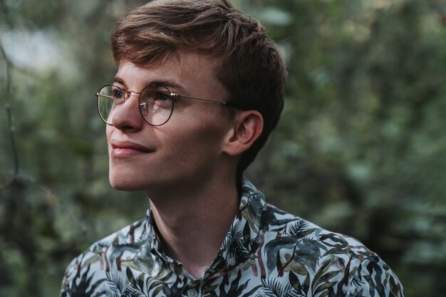 Portrait of a young Caucasian male with eyeglasses looking aside in a garden