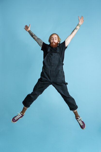 Portrait of young caucasian man looks dreamful, cute and happy. Jumping. laughting on blue  space