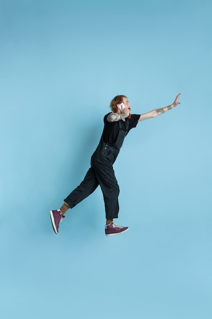 Portrait of young caucasian man looks dreamful, cute and happy. Jumping. laughting on blue studio background. Copyspace for your advertising. Concept of future, target, dreams, visualisation.