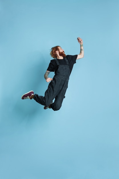 Free photo portrait of young caucasian man looks dreamful, cute and happy. jumping. laughting on blue studio background. copyspace for your advertising. concept of future, target, dreams, visualisation.