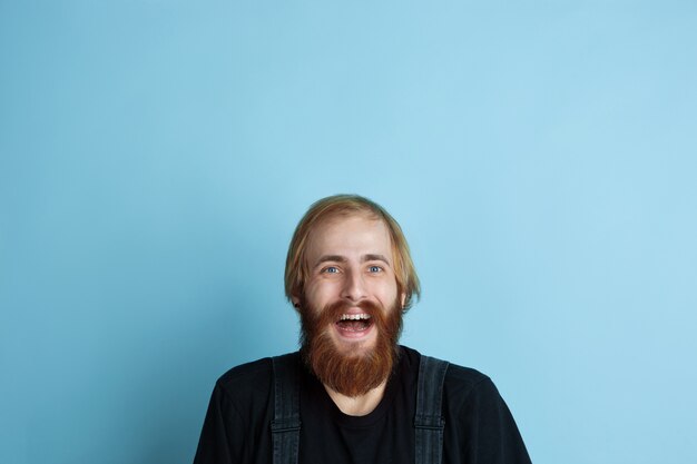 Portrait of young caucasian man looks dreamful, cute and happy. Looking up and thinking on blue  space