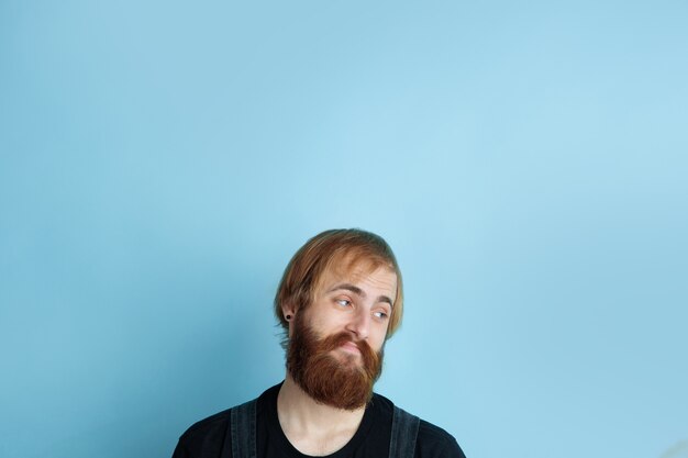 Portrait of young caucasian man looks dreamful, cute and happy. Looking up and thinking on blue studio background. Copyspace for your advertising. Concept of future, target, dreams, visualisation.