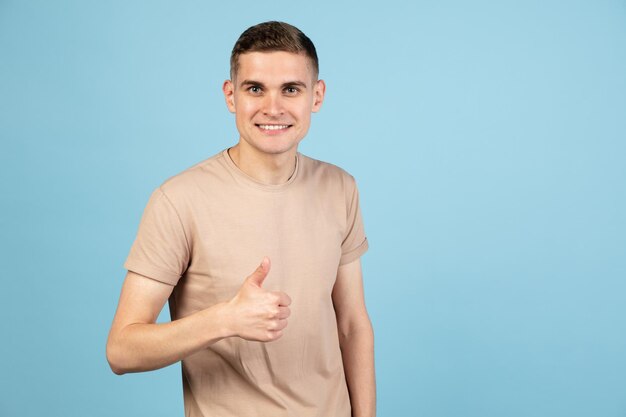 Portrait of young Caucasian man posing isolated over blue studio background with copyspace for ad Concept of human emotions