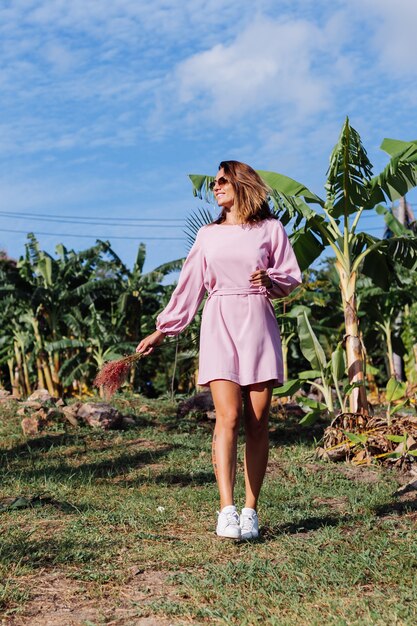 Portrait of young caucasian tanned woman in romantic pink dress round earings silver bracelet and sunglasses