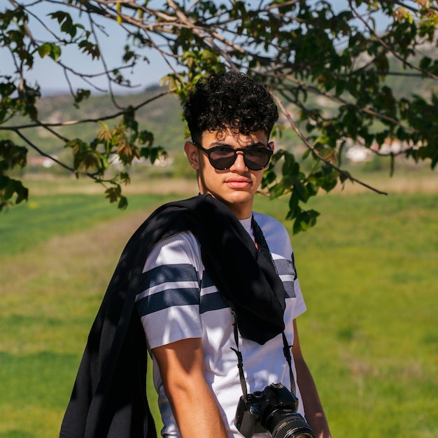 Portrait of young charming man wearing sunglasses and digital camera looking at camera