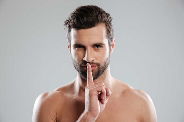 Portrait of a young charming naked man showing silence gesture