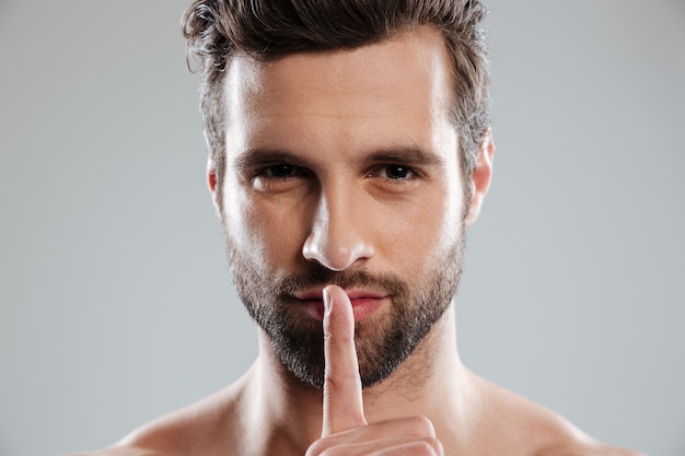 Portrait of a young charming naked man showing silence gesture