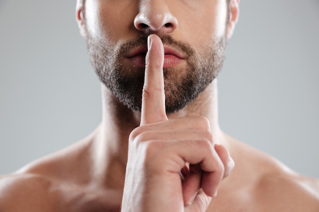 Portrait of a young charming naked man showing silence gesture