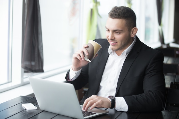 Free photo portrait of young cheerful businessman working at wooden table in modern coffee shop