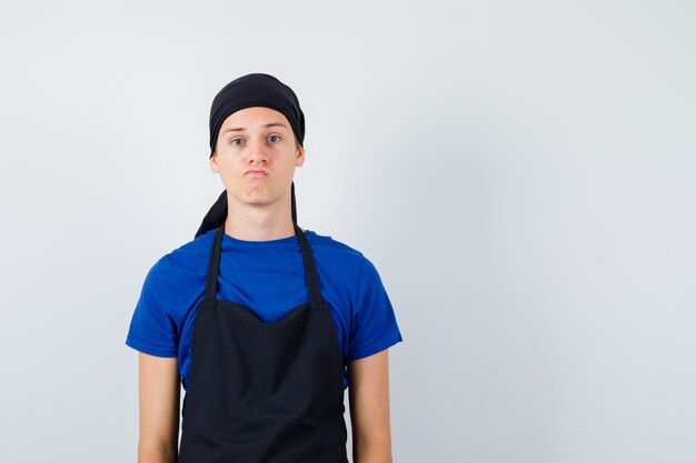 Portrait of young cook man posing while standing in t-shirt, apron and looking hesitant front view