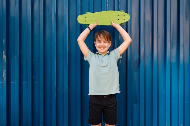 Ritratto giovane ragazzo sorridente cool in polo blu in posa con penny board nelle mani