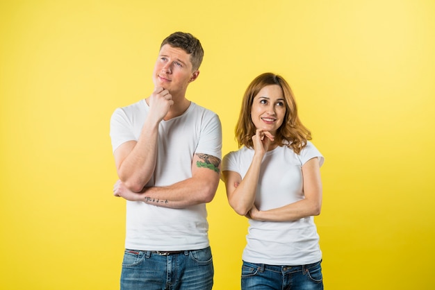 Portrait of a young couple daydreaming against yellow background